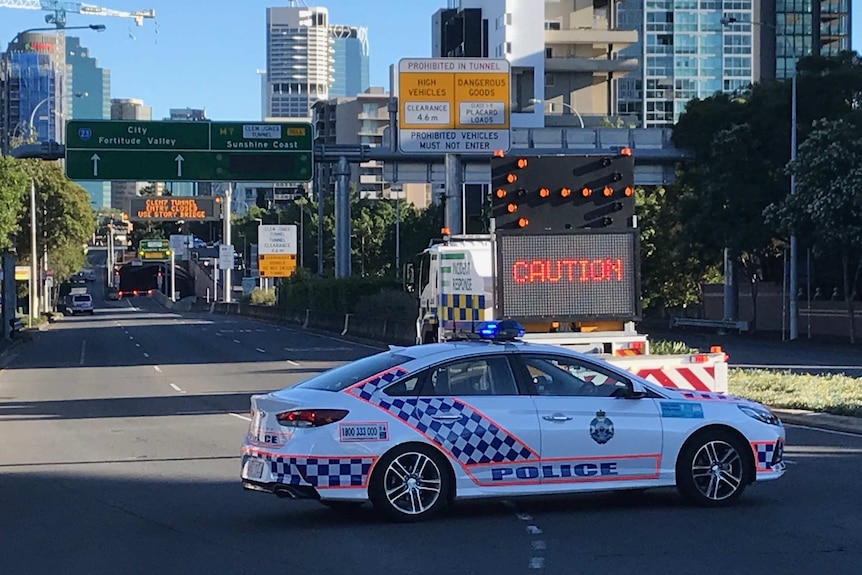 A police car is parked across the road, blocking the entrance to the Clem 7 tunnel in the Brisbane CBD, next to a caution sign