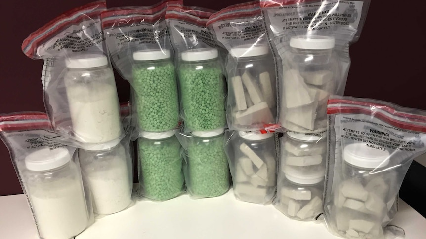 Drugs including ecstasy tablets, heroin and cocaine in plastic tubs inside 12 zip lock bags on a table.