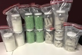 Drugs including ecstasy tablets, heroin and cocaine in plastic tubs inside 12 zip lock bags on a table.