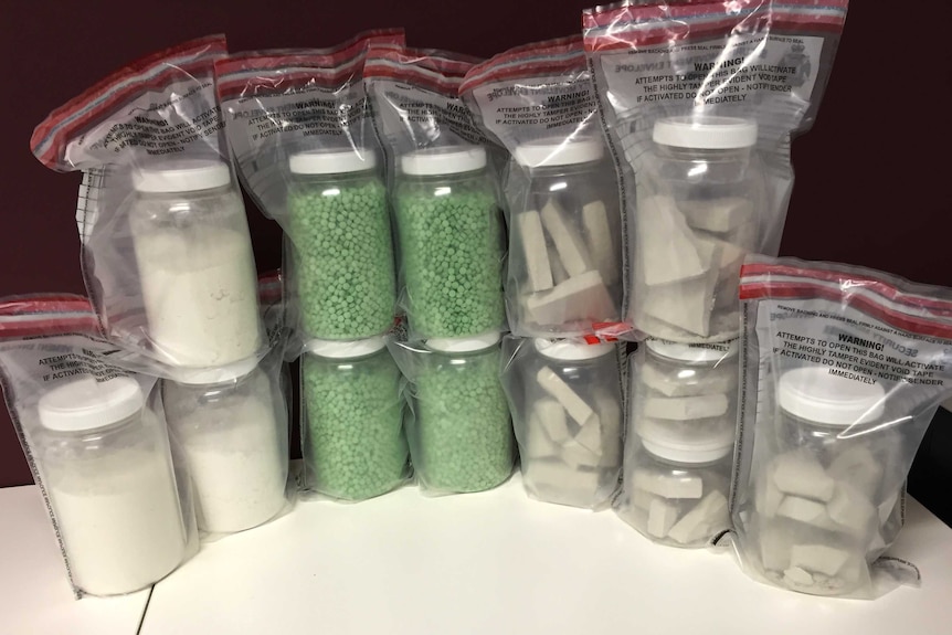 Drugs including ecstacy tablets, heroin and cocaine in plastic tubs inside 12 zip lock bags on a table.