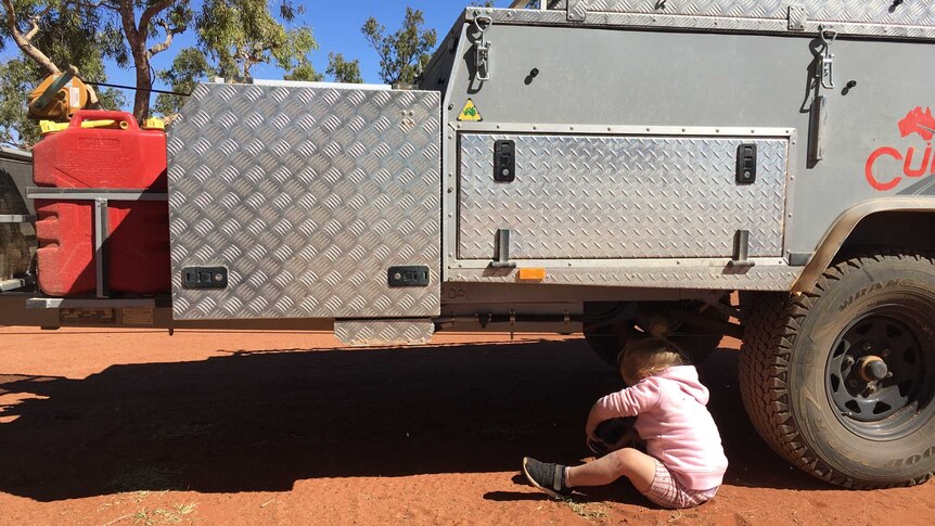 Two-year-old Paige sits underneath the Mifflin family's camper trailer.