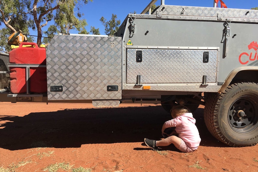 Two-year-old Paige sits underneath the Mifflin family's camper trailer.