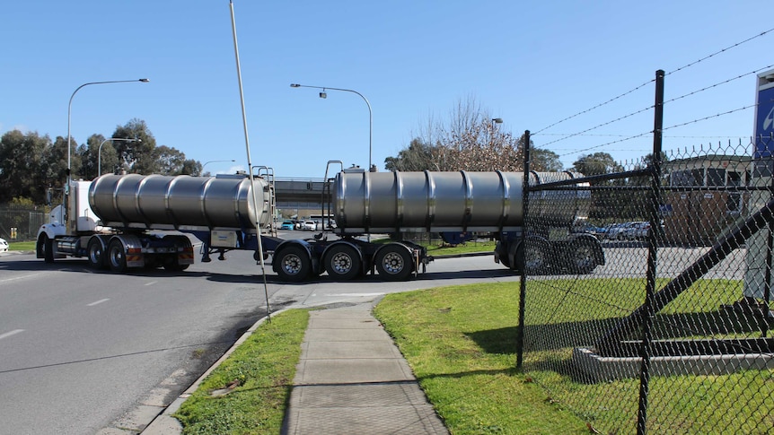 A water tanker drives out of a factory driveway and onto a road