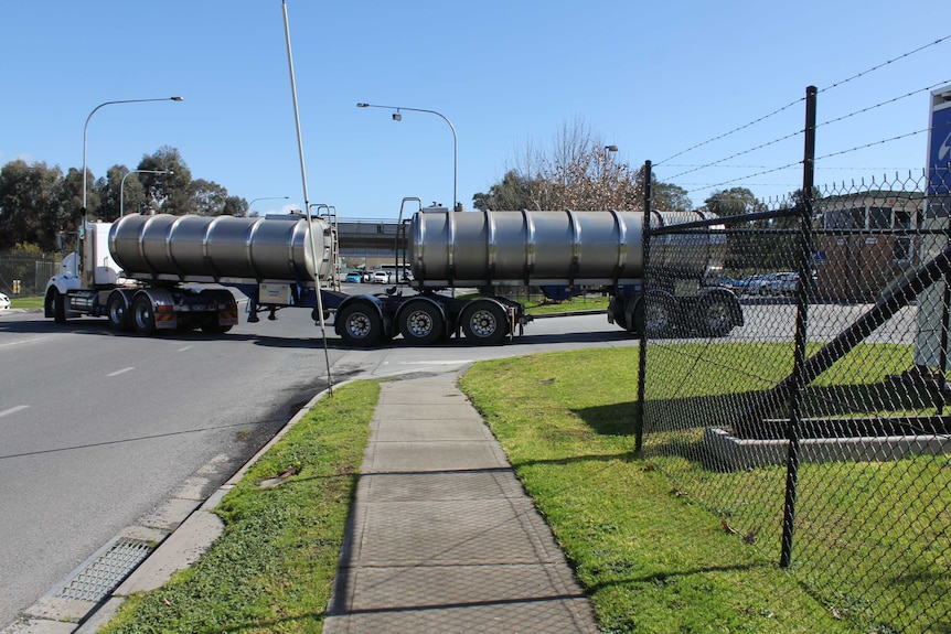 A water tanker drives out of a factory driveway and onto a road