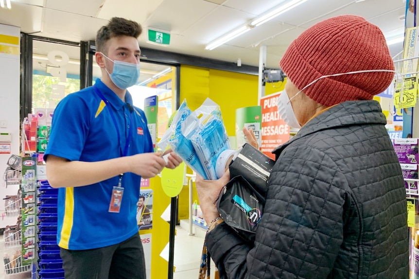 A woman wearing a red beanie holds two packets of blue surgical masks inside a Chemist Warehouse store.
