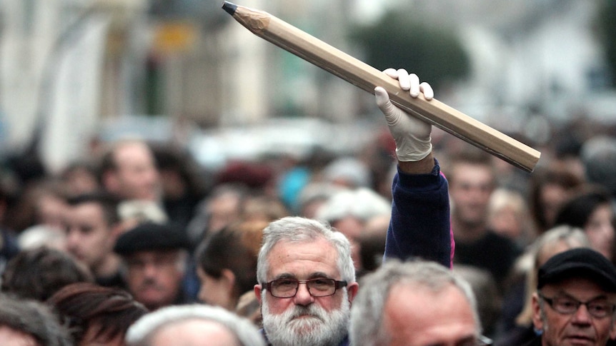 A man at a rally holds a giant pencil in the air