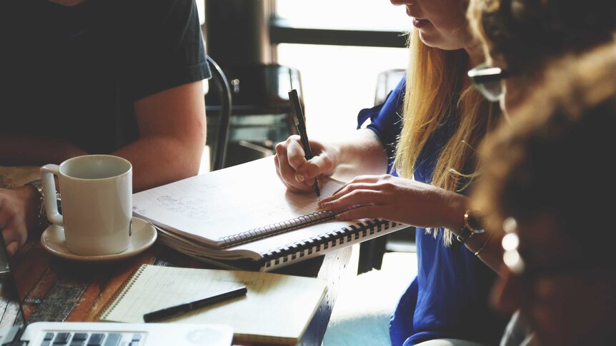 A group of people making a list near coffee and a laptop.