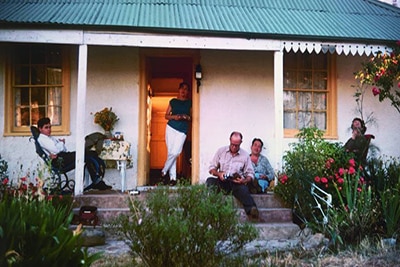 A group of people sit on a verandah at sunset.