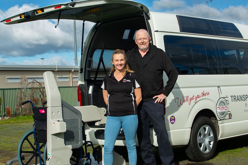 A woman and man standing in front of van with a wheelchair seated on the rear-mounted wheelchair lift.