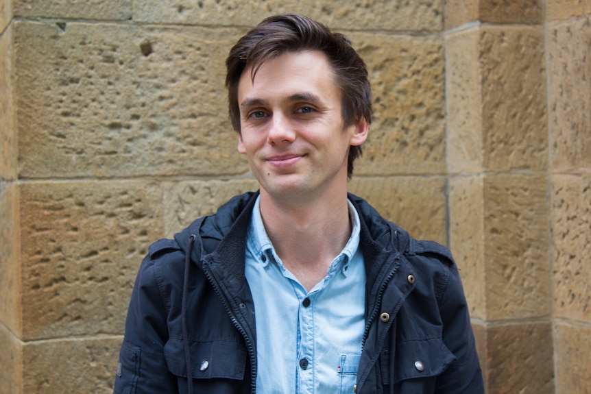 Colour photograph of Anglican assistant minister Matt Aroney standing in front of a sandstone wall.