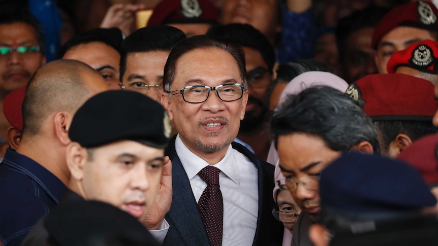 Anwar Ibrahim is surrounded by a press back and police as he leaves hospital.