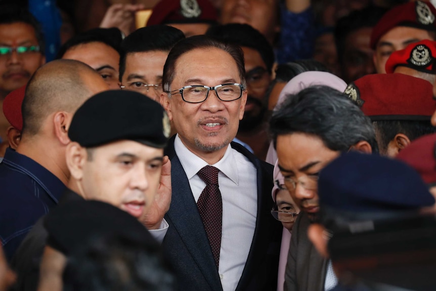 Anwar Ibrahim is surrounded by a press back and police as he leaves hospital.