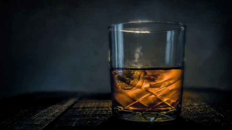 Picture of a glass of whisky on a table. The background in dark. 