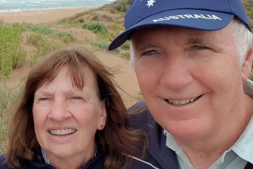 Selfie of older couple smiling with beach and dunes in the background