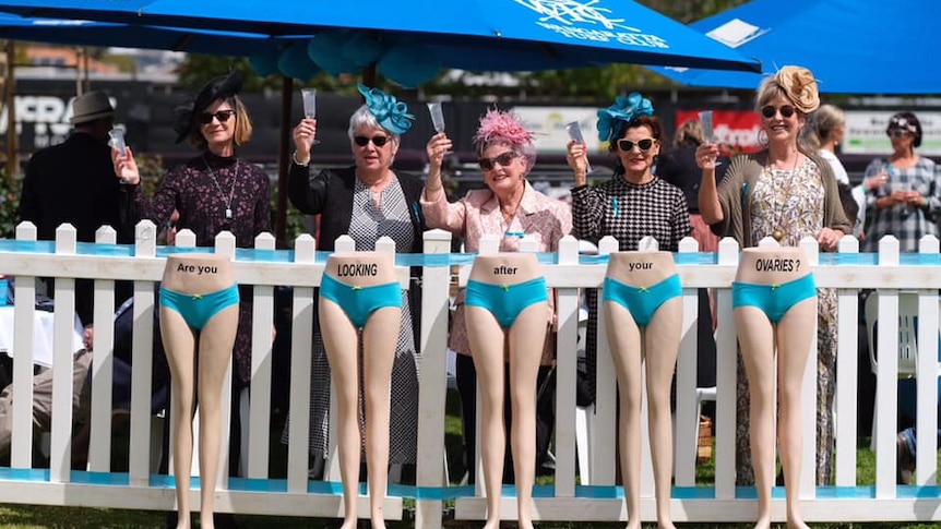 A group of women stand behind mannequins wearing teal undies that say Are you looking after your ovaries?