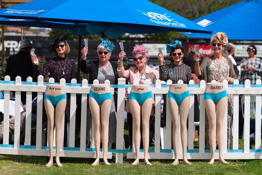 A group of women stand behind mannequins wearing teal undies that say Are you looking after your ovaries?