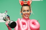 Miley Cyrus wears a pink figure hugging dress with Do It written in inflatable letters on the front.