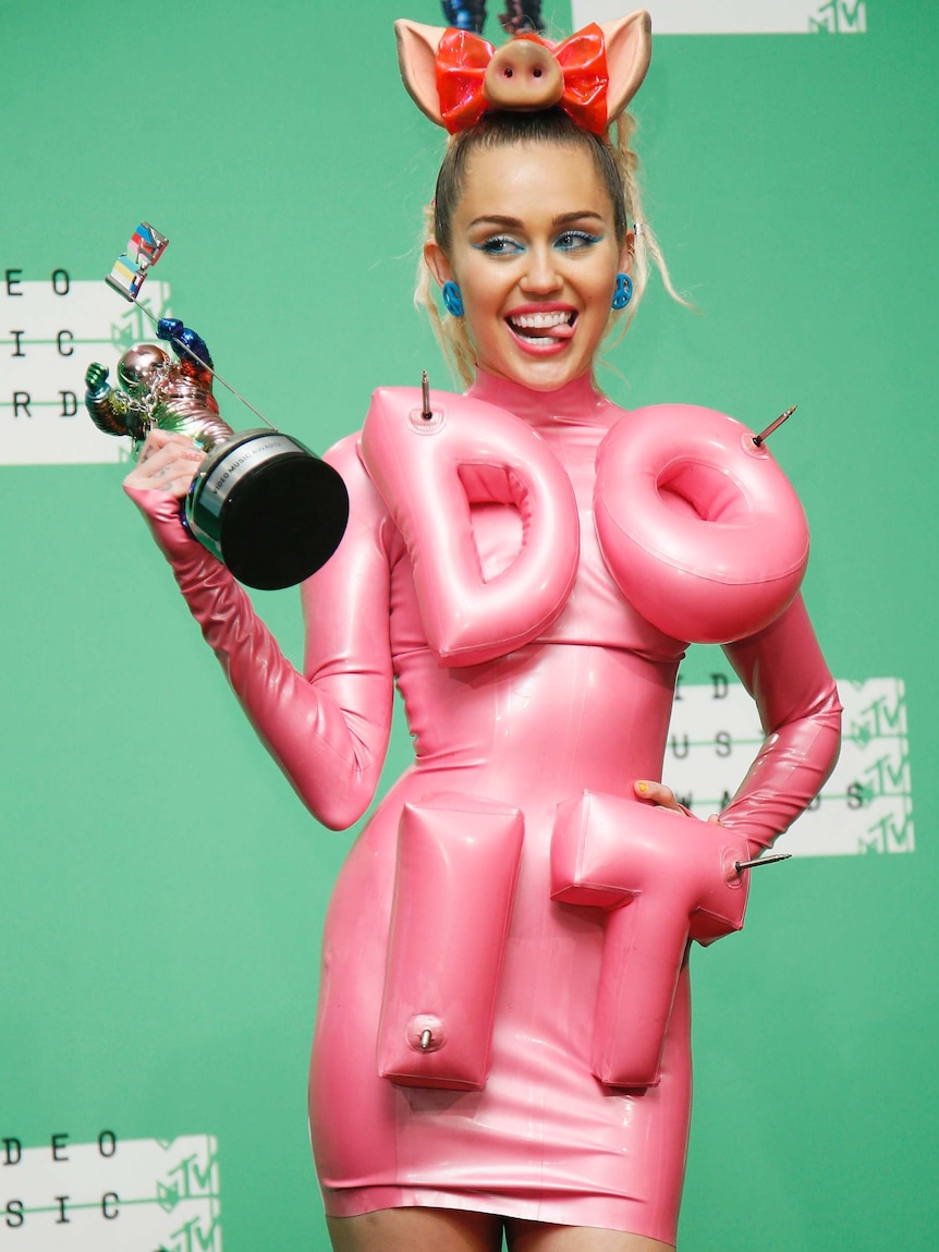 Miley Cyrus wears a pink figure hugging dress with Do It written in inflatable letters on the front.