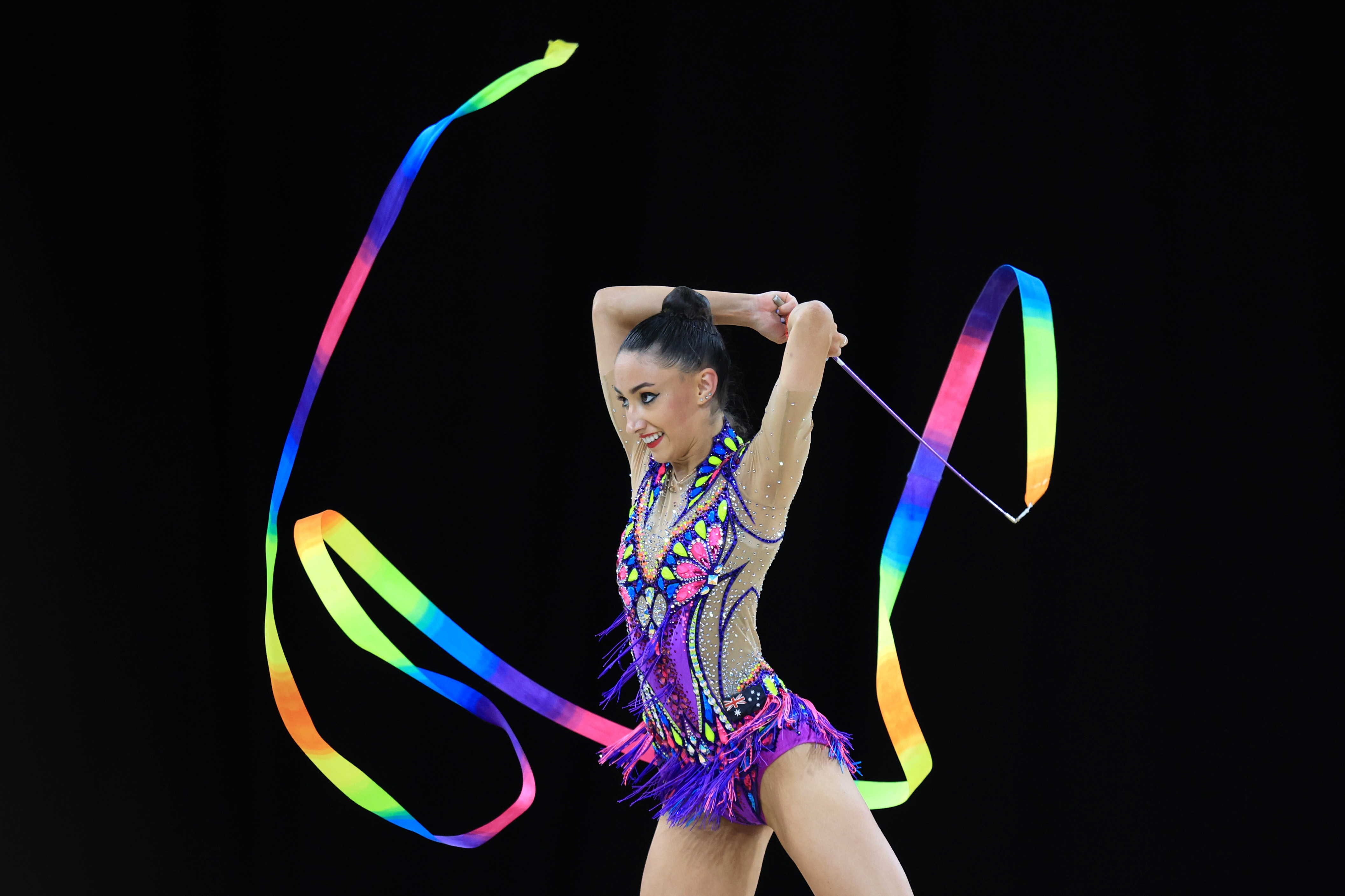 A woman holds a ribbon and smiles while twirling it in the air.