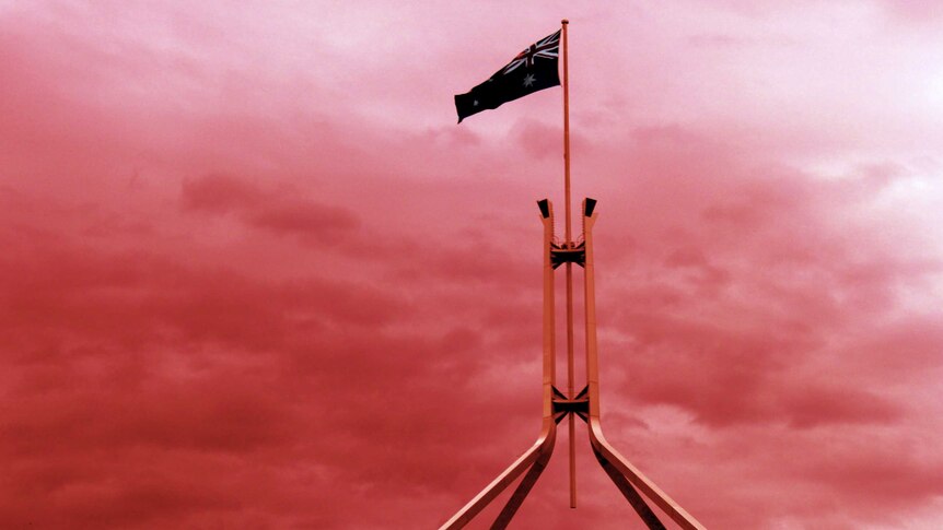 Parliament House's flagpole with an Australian flag flying and a red sky behind it.