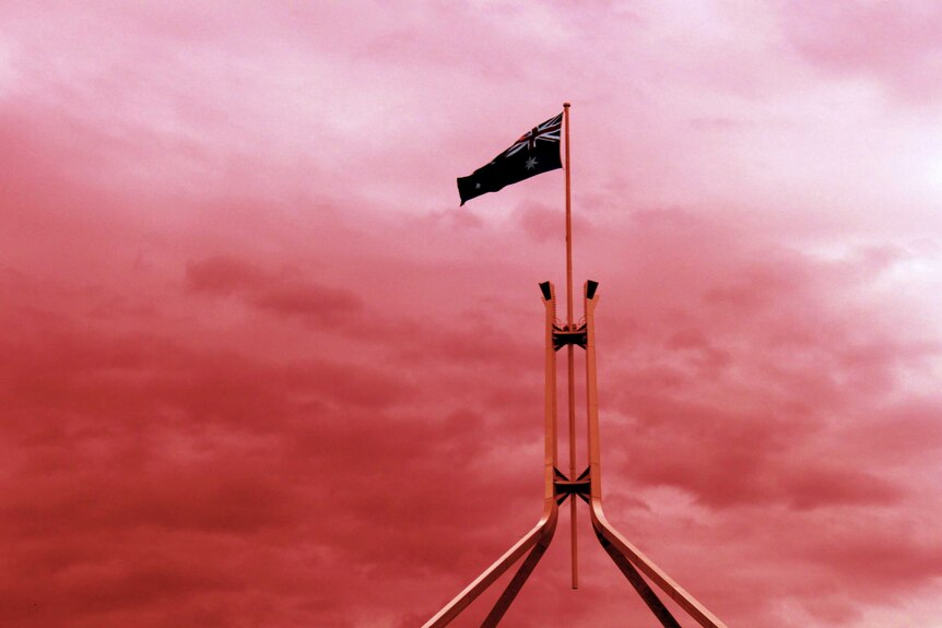 Parliament House's flagpole with an Australian flag flying and a red sky behind it.