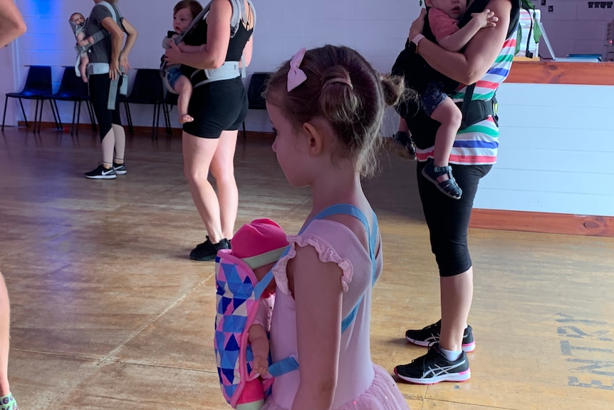 Six year old girl Mary Myers and her doll in a pouch joining Mums in baby-friendly dance class