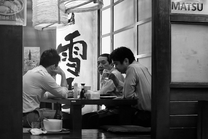 A black and white photo of three Japanese men having a drink after work.