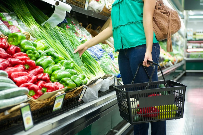一位身穿绿色上衣和牛仔裤的女购物者在超市里查看蔬菜。