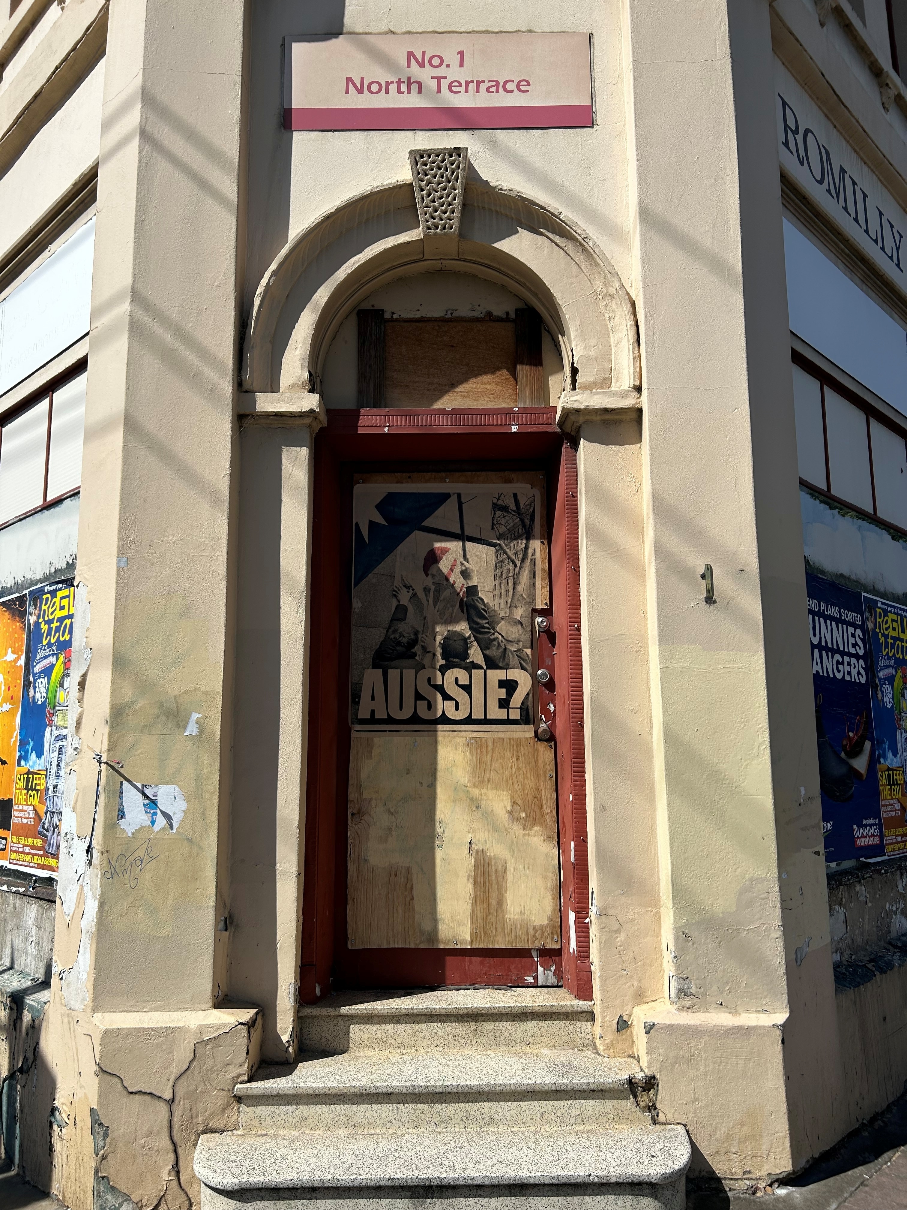 Uma placa com vinhetas na porta de um prédio antigo com pessoas derrubando uma placa com as palavras Aussie? abaixo dele