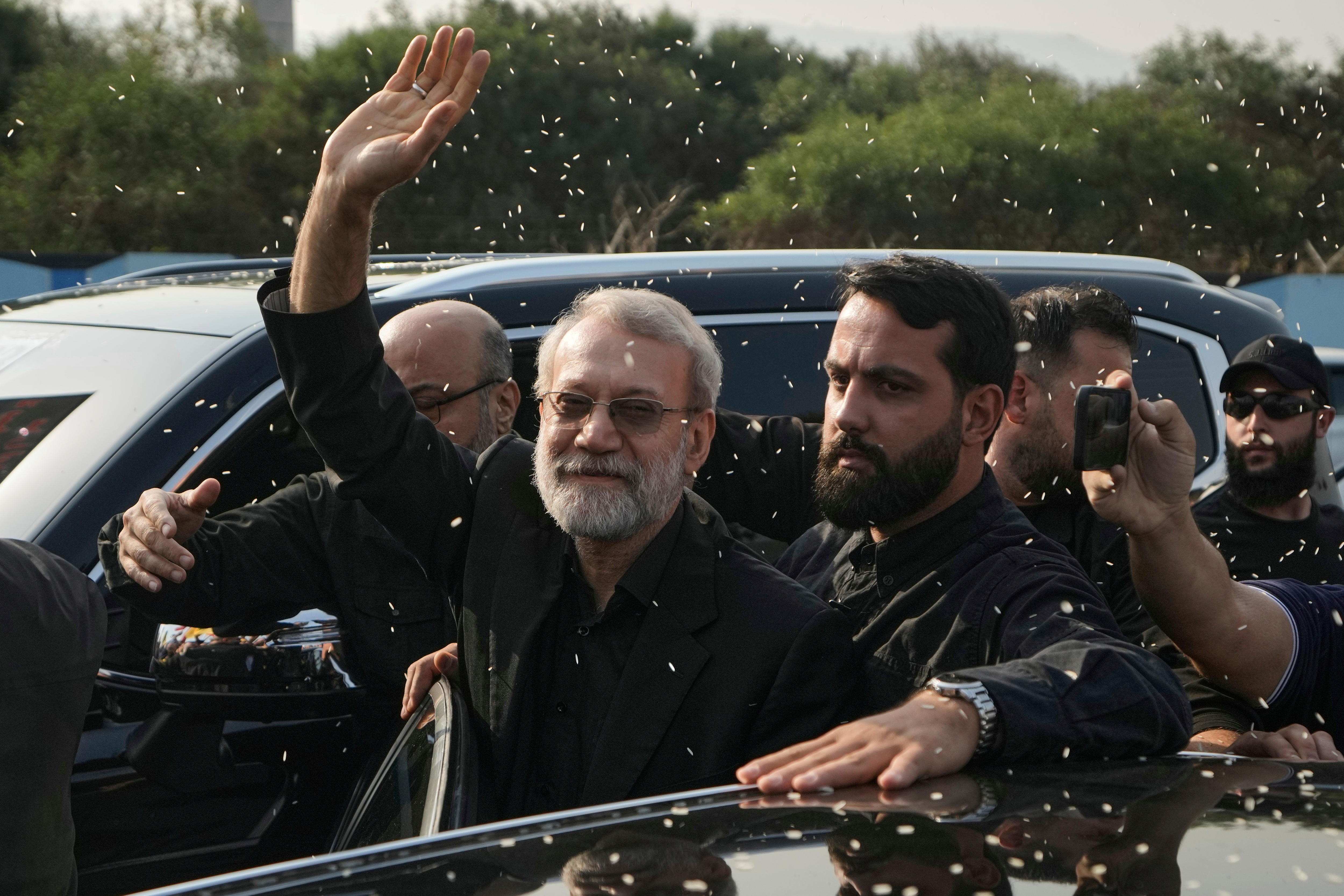 Ali Larijani waving as rice is thrown at him with several people behind him.