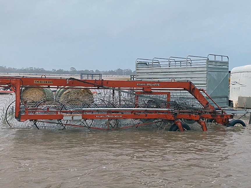 A red hay rake is submerged up to the top of its wheels in flood water.