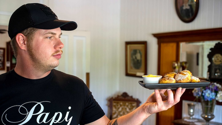 A man wearing a black t-shirt holds up a plate of pumkpin scones
