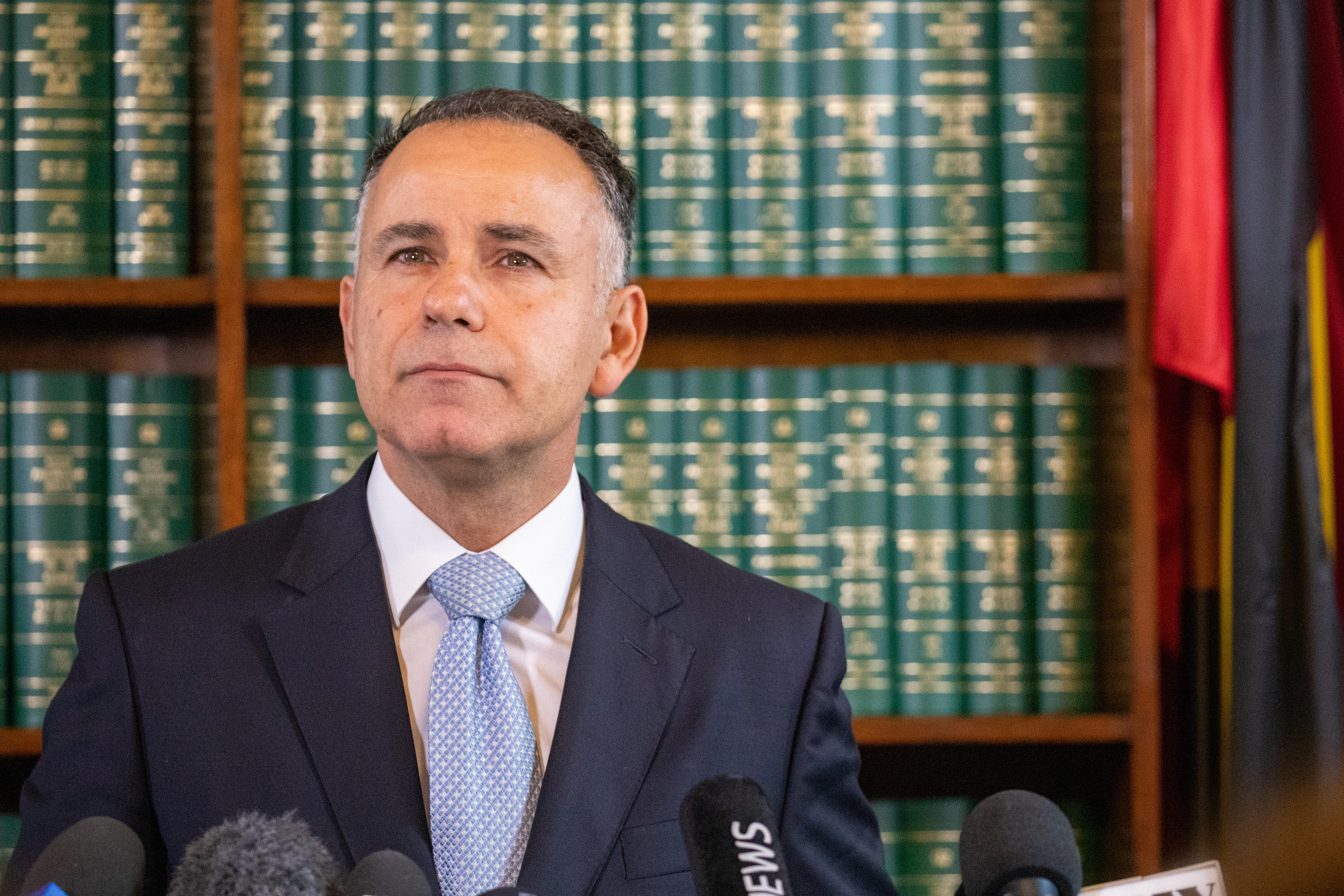 John Pesutto looks up in a determined fashion, standing in front of a shelf of books inside Parliament House.