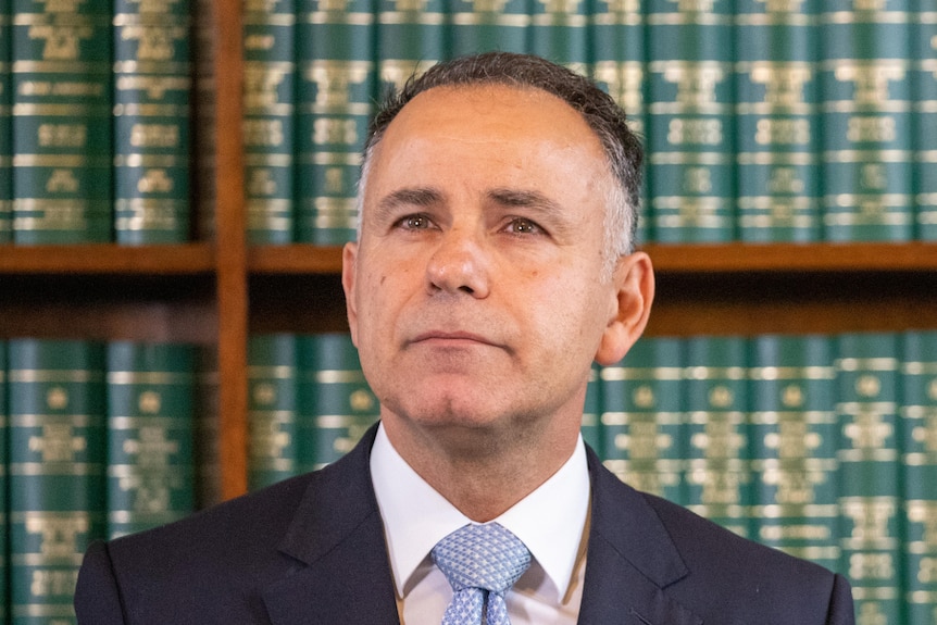 John Pesutto looks up in a determined fashion, standing in front of a shelf of books inside Parliament House.