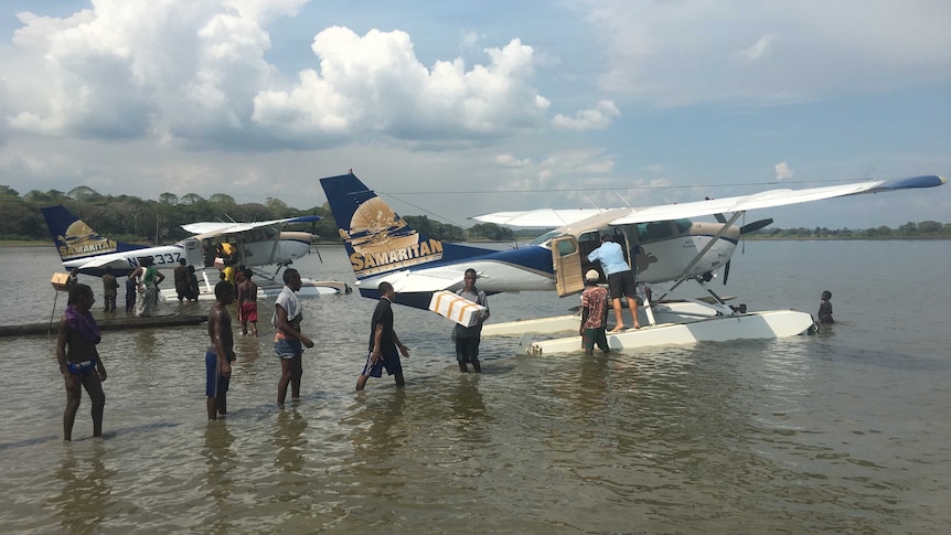 Villagers line up to help unload boxes from two floatplanes landed on the river