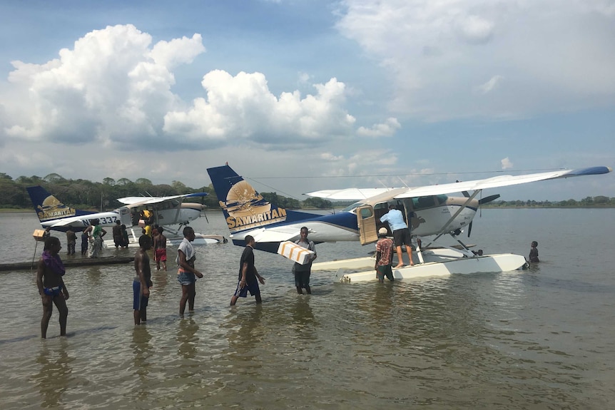 Villagers line up to help unload boxes from two floatplanes landed on the river