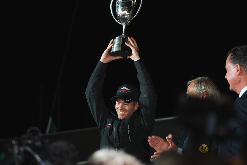 A man hoists a silver cup trophy above his head.