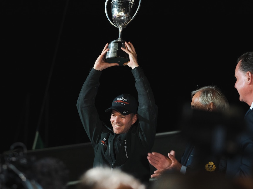 A man hoists a silver cup trophy above his head.