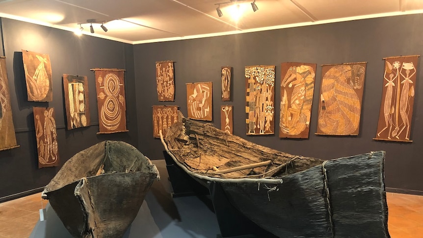 The bark canoes sit in the middle of the room, other art is hung on the walls