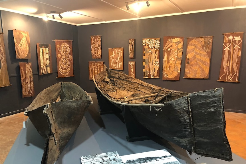 The bark canoes sit in the middle of the room, other art is hung on the walls