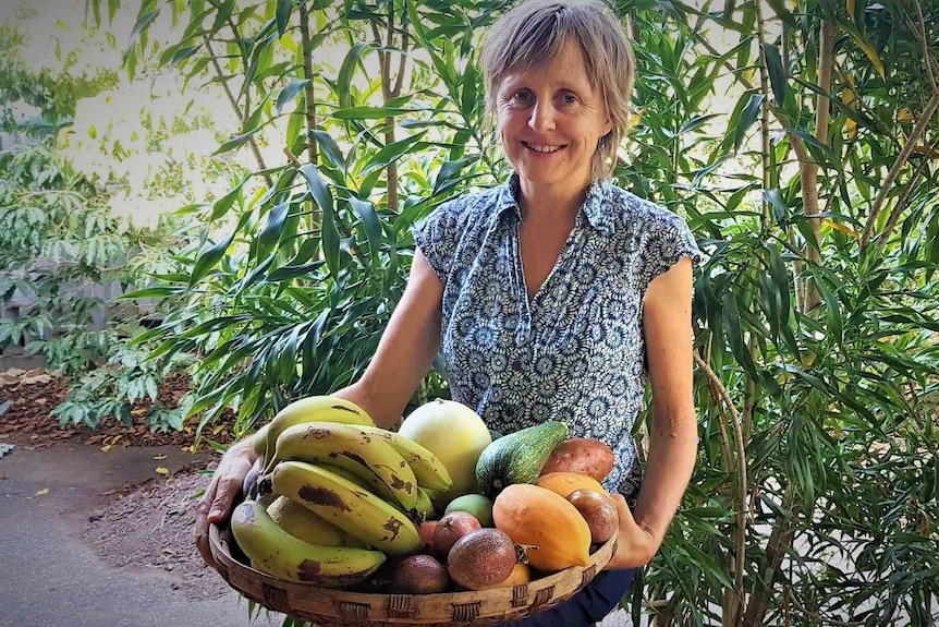 4:3 ratio of woman in garden smiling posed holding wide basket of vegetables and fruit