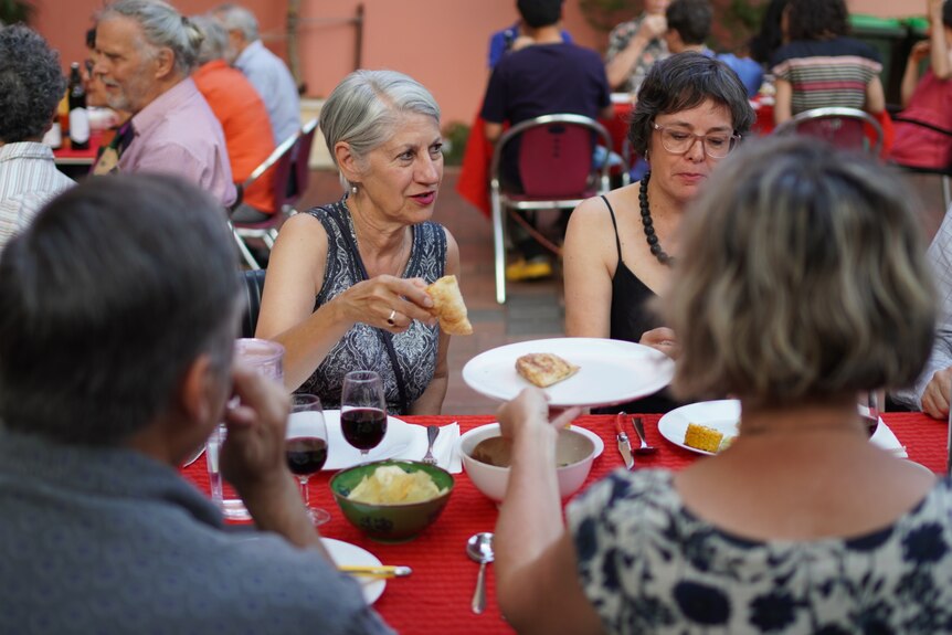 Two women and other people facing away from the camera having a meal outside
