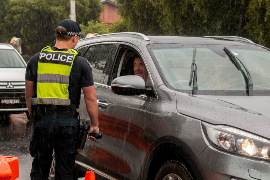 A police officer talking to a driver in a grey 4WD while it's raining heavily.
