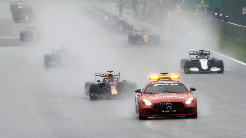 Formula One cars in the rain driving behind the safety car.