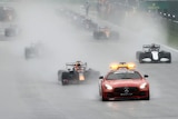 Formula One cars in the rain driving behind the safety car.