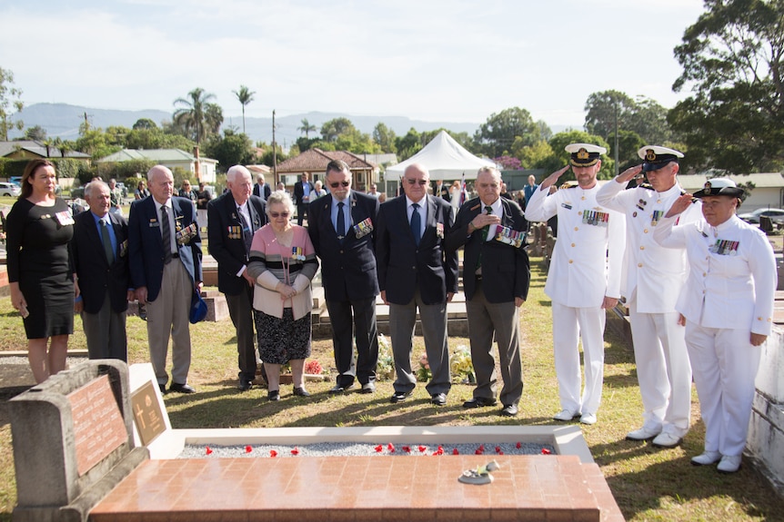 A group of servicemen stand saluting around the grave of an Indigenous soldier at a NSW cemetery.