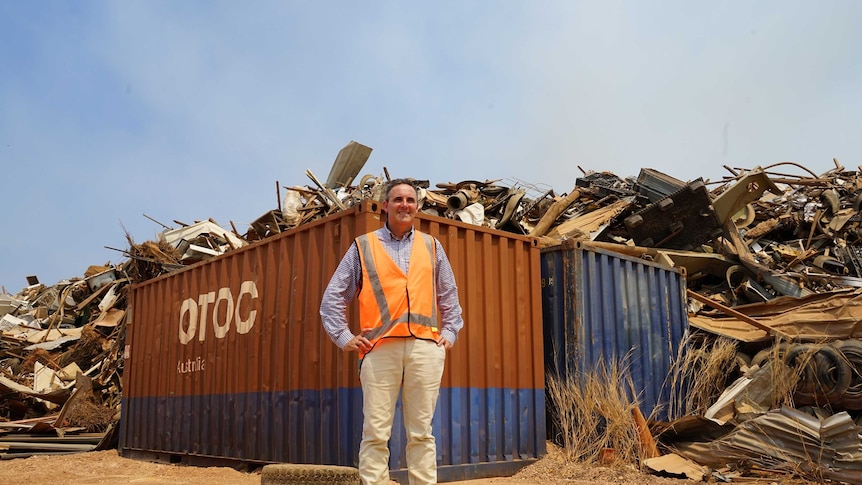 Nik Kleine is wearing an orange vest and is smiling at the camera. He is standing next to a large container full of rubbish.