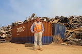 Nik Kleine is wearing an orange vest and is smiling at the camera. He is standing next to a large container full of rubbish.
