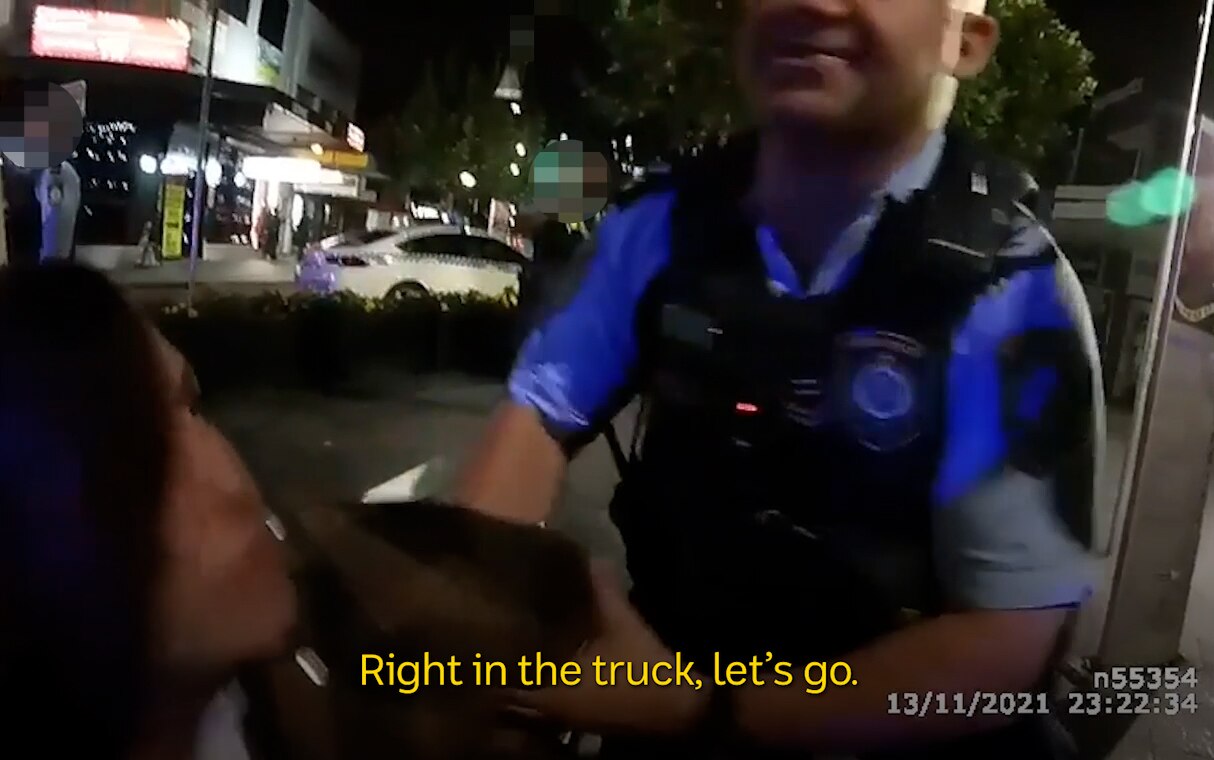 A still of body-worn video, showing a man being grabbed by a police officer at night.