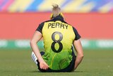 Ellyse Perry's name and number is visible on the back of her Australian jersey as she sits on the ground after being injured.